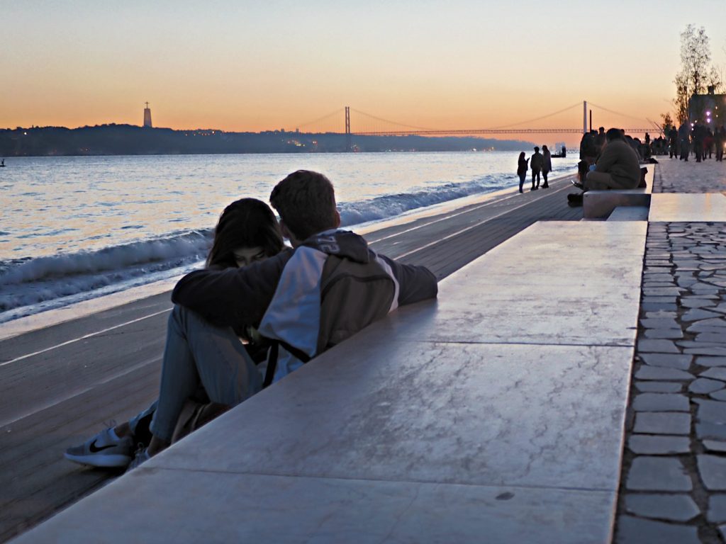 A couple looking at the sunset over the 25th of April bridge in Lisbon, Portugal